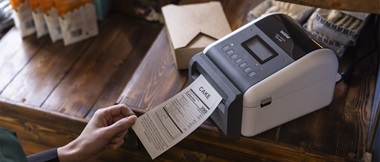 Label printer on a table with a woman's hand collecting the linerless printed label