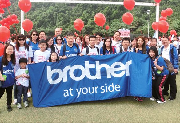 Crowd of people holding a Brother banner with red balloons in the background