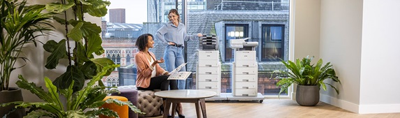 Two women in large office, two Brother printers, plants, window, table