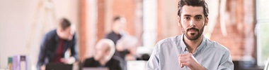 Man wearing shirt in office, people in background talking