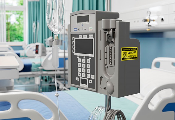 Yellow maintenance label on side of IV infusion pump in hospital ward next to bed